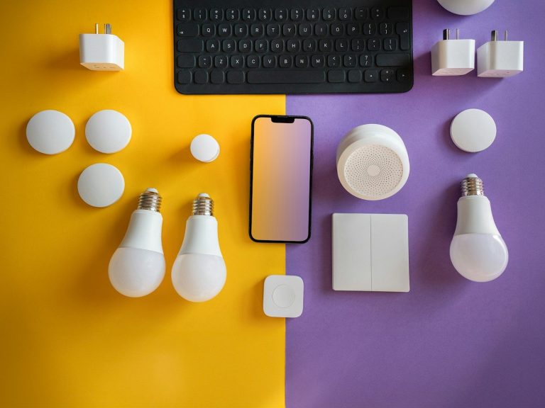 AMK IT Solutions Smart devices and accessories arranged on a yellow and purple background, including bulbs and a phone.